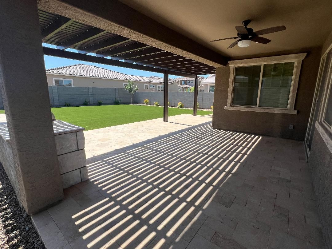Covered patio with striped shadows, overlooking a grassy backyard.