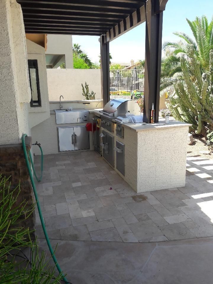 Outdoor kitchen with grill, sink, and cabinets under a wooden pergola.