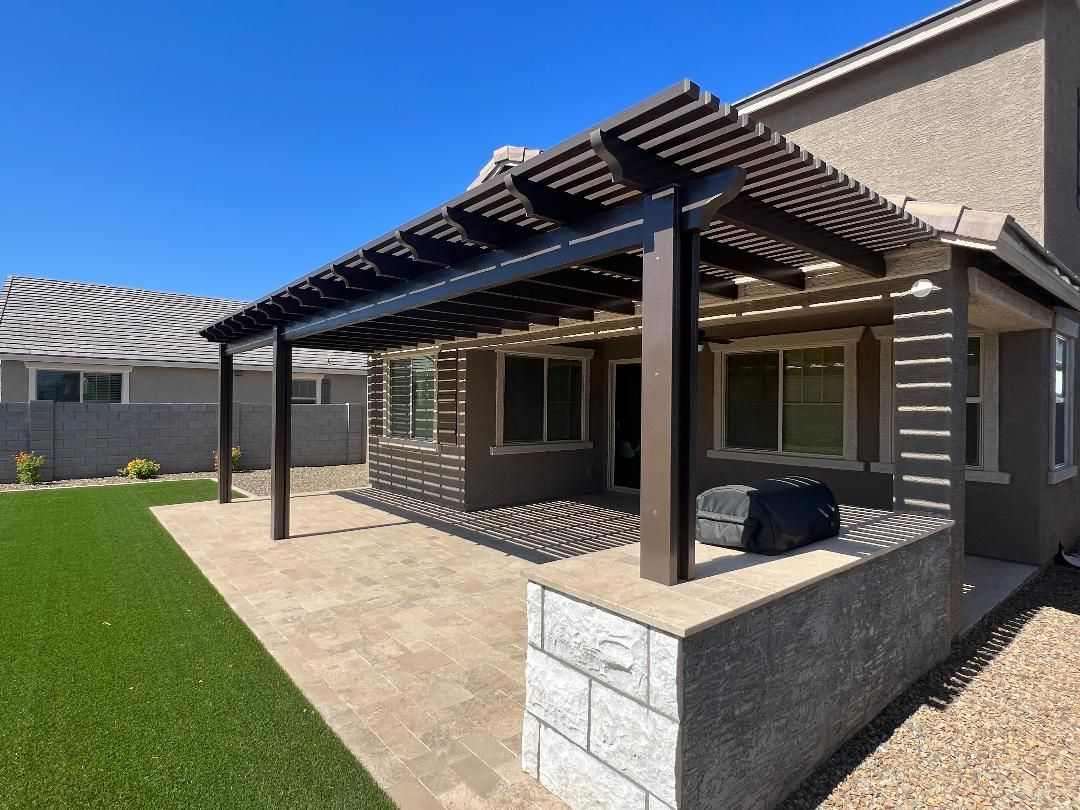 Patio with pergola, concrete flooring, and a low wall, next to a house with windows.