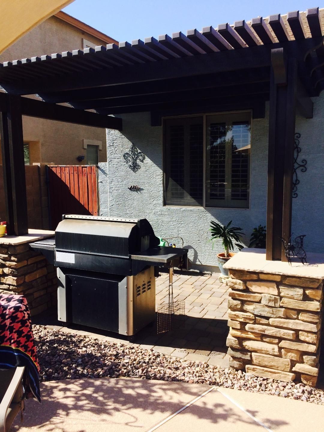 A backyard with a pergola, built-in grill, and stone columns.