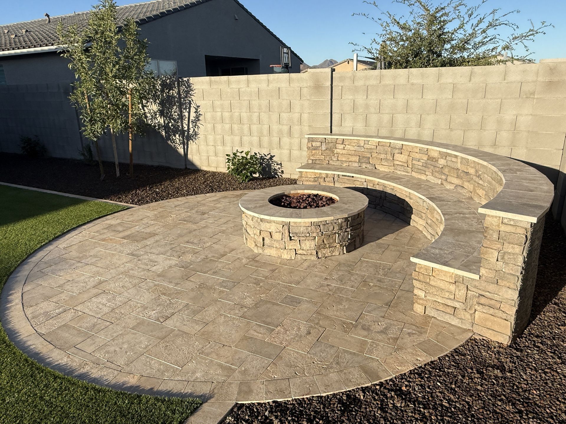 Circular stone patio with fire pit, built-in curved seating, and concrete block wall.