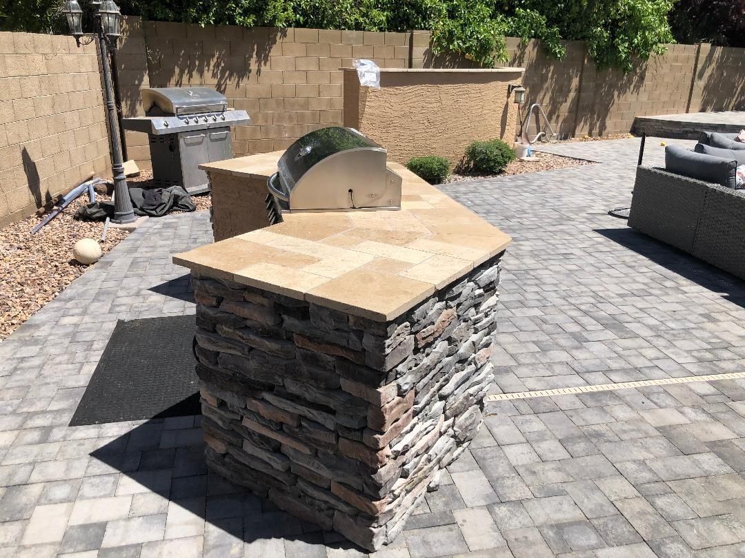 Outdoor kitchen with stacked stone base and countertop, grill, and paved patio.