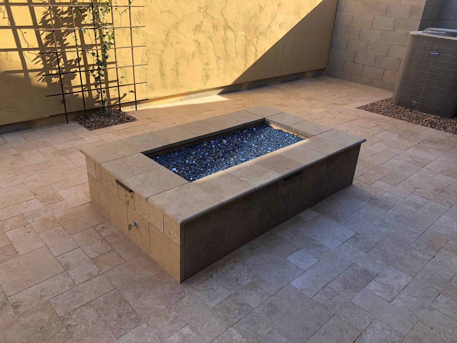 Rectangular beige fire pit on a stone patio with dark blue fire glass.