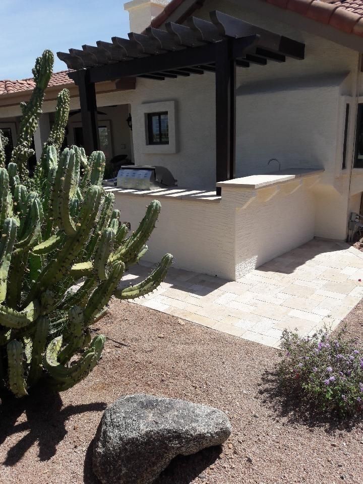 Outdoor kitchen with a cactus, stone patio, and dark wood pergola.