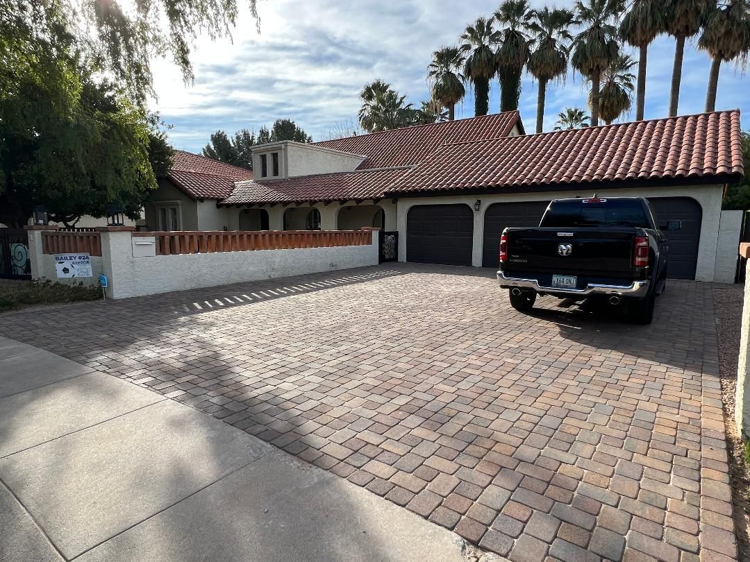 House with red tile roof, brick driveway, black truck parked in front of garage. Palm trees in the background.