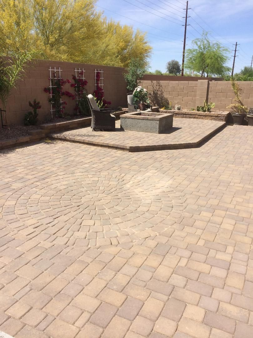 Brick patio with fire pit, plants, and tan stucco walls. Sunny outdoor setting.