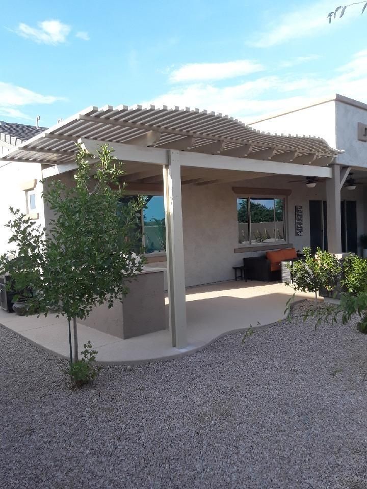 Patio with beige pergola, beige house, and small tree on gravel.