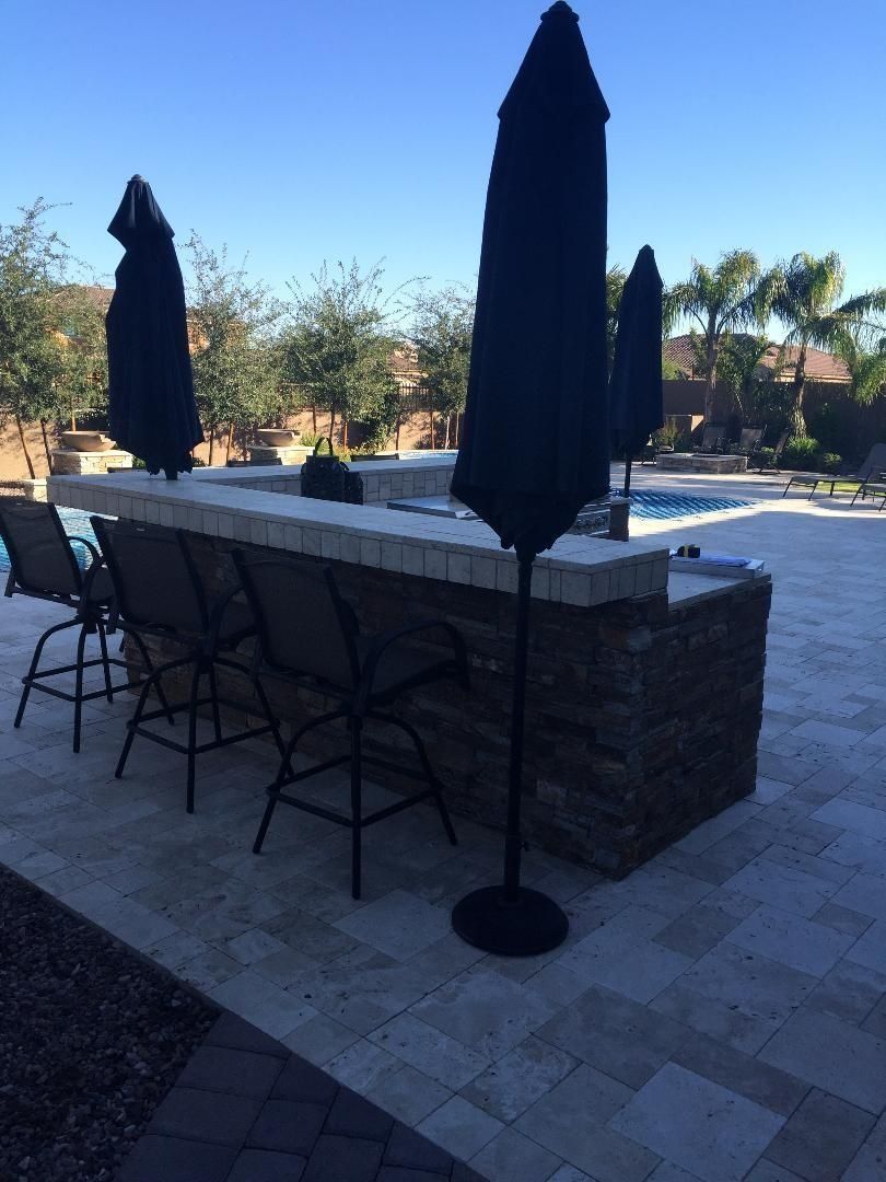 Outdoor bar area with bar stools, umbrellas, and swimming pool.