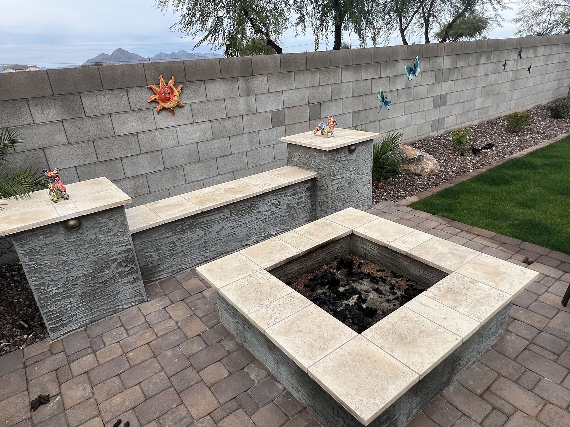 Backyard with fire pit, seating, and decorative wall with sun and bird art.