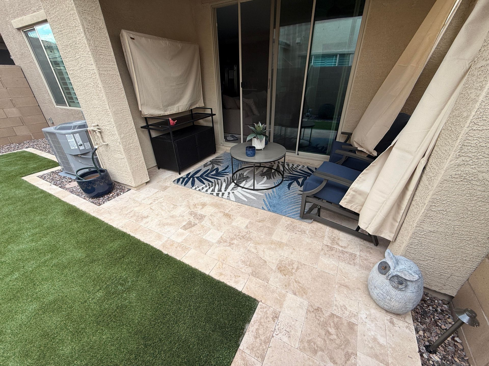 Patio with artificial grass, tan tile, furniture, and a rug. Sliding glass door and air conditioning unit.