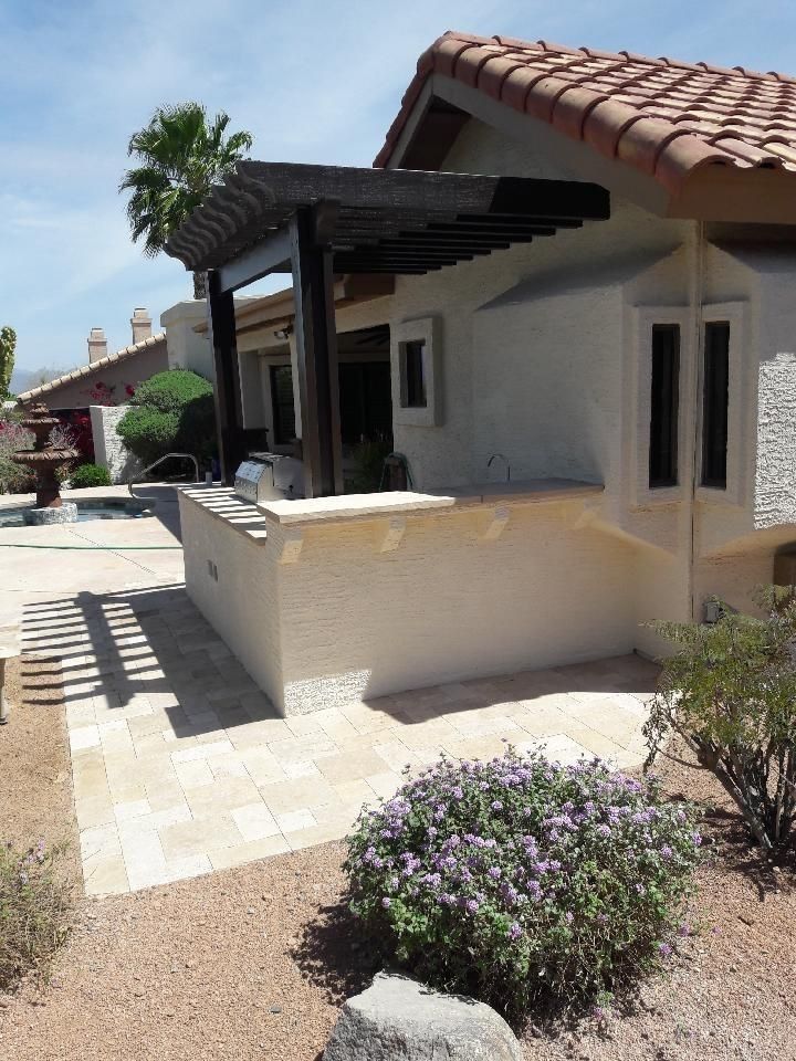 Outdoor patio with pergola, stucco wall, and tile pathway, beside a swimming pool.