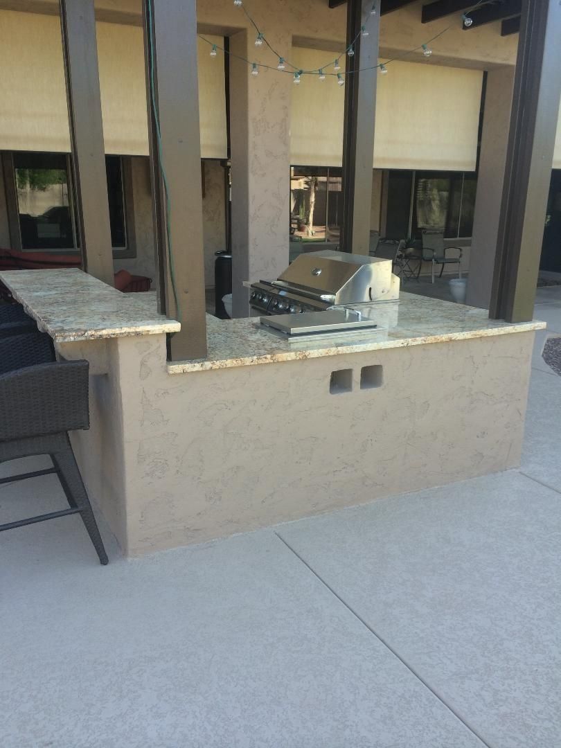 Outdoor kitchen with granite countertop, built-in grill, and bar seating.