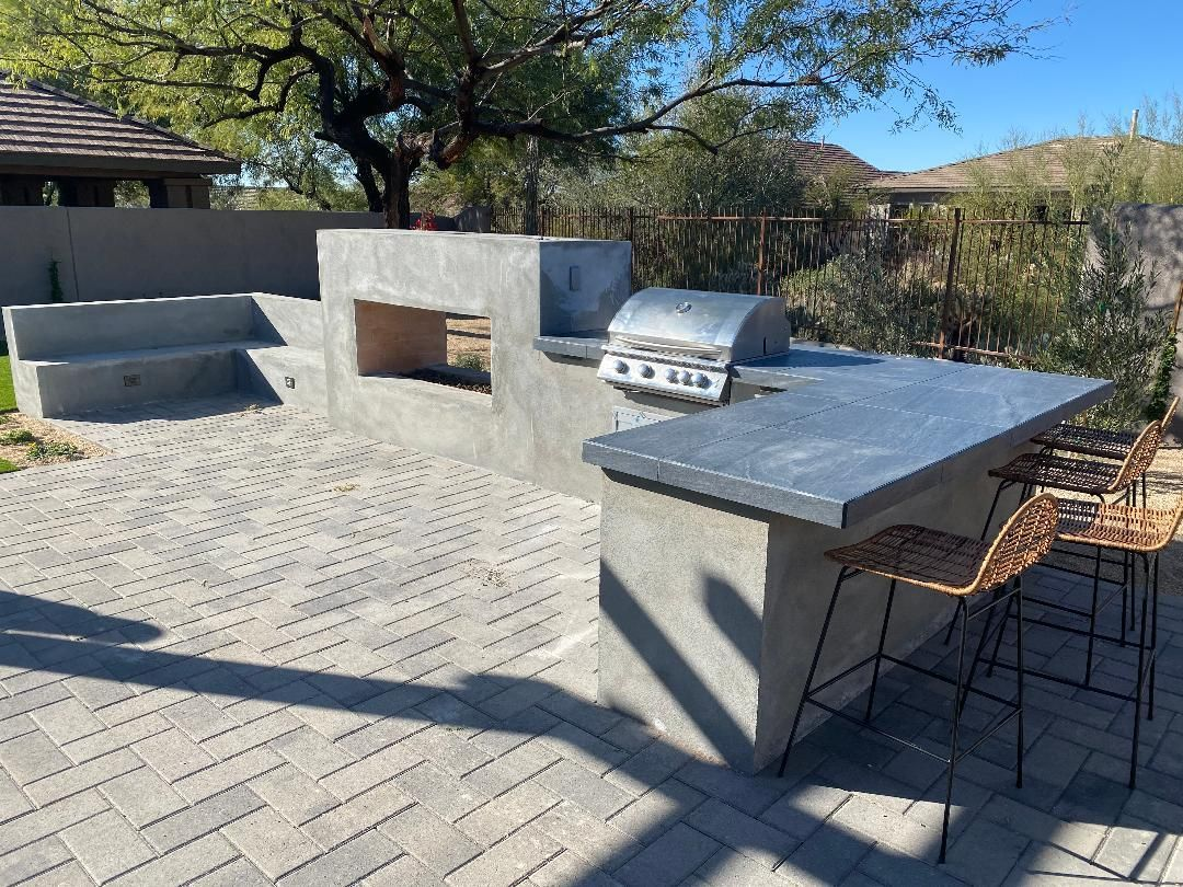 Outdoor concrete grilling station with built-in grill, counter, seating, and brick patio.