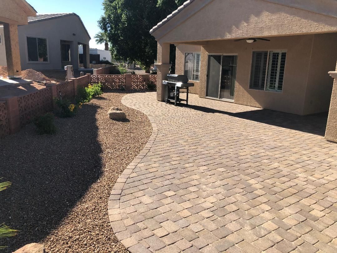 Brick patio and gravel landscaping beside a tan stucco house with a sliding glass door and grill.