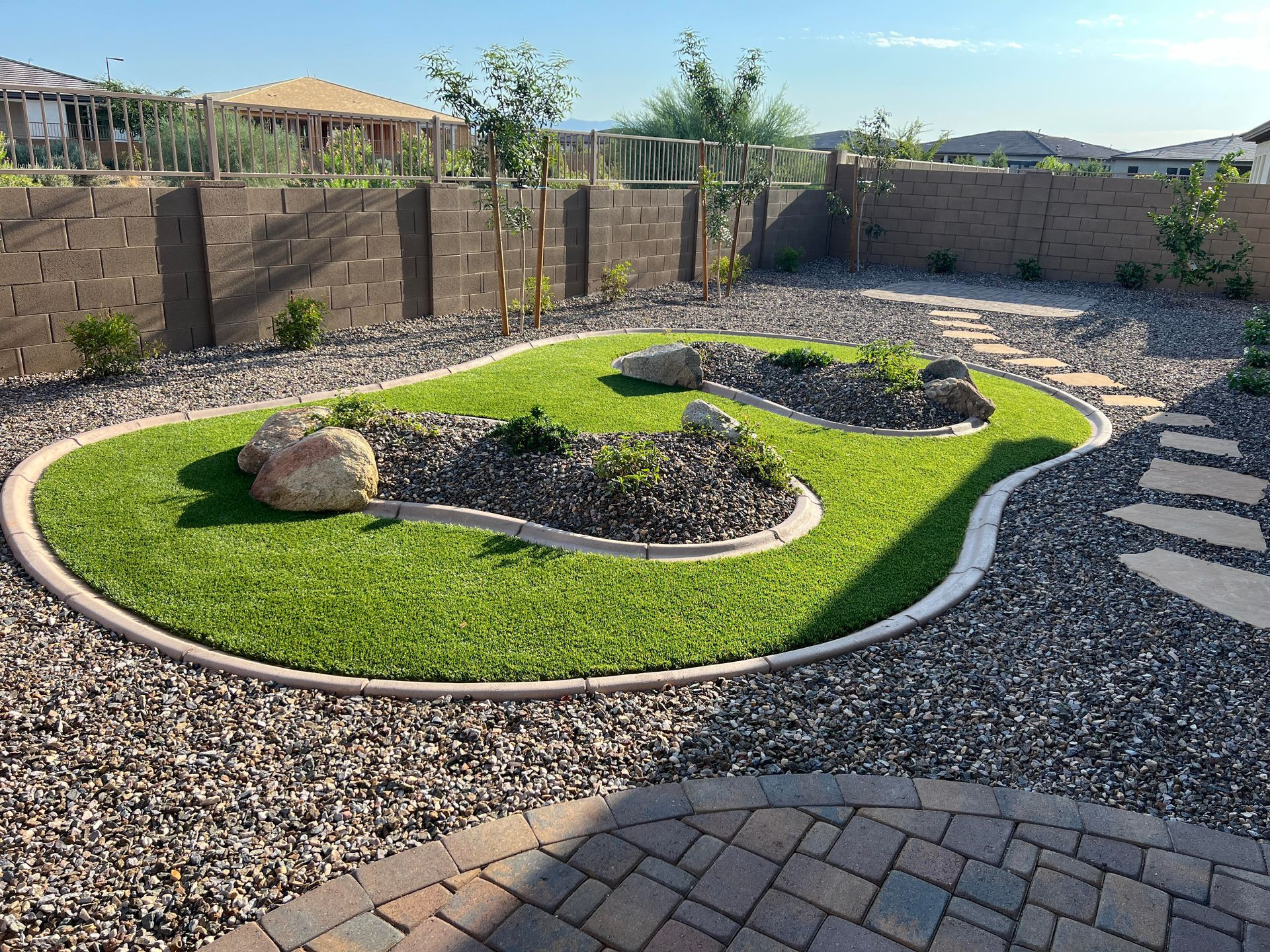 Backyard with artificial turf lawn, rock garden, stone path, and retaining walls under a blue sky.