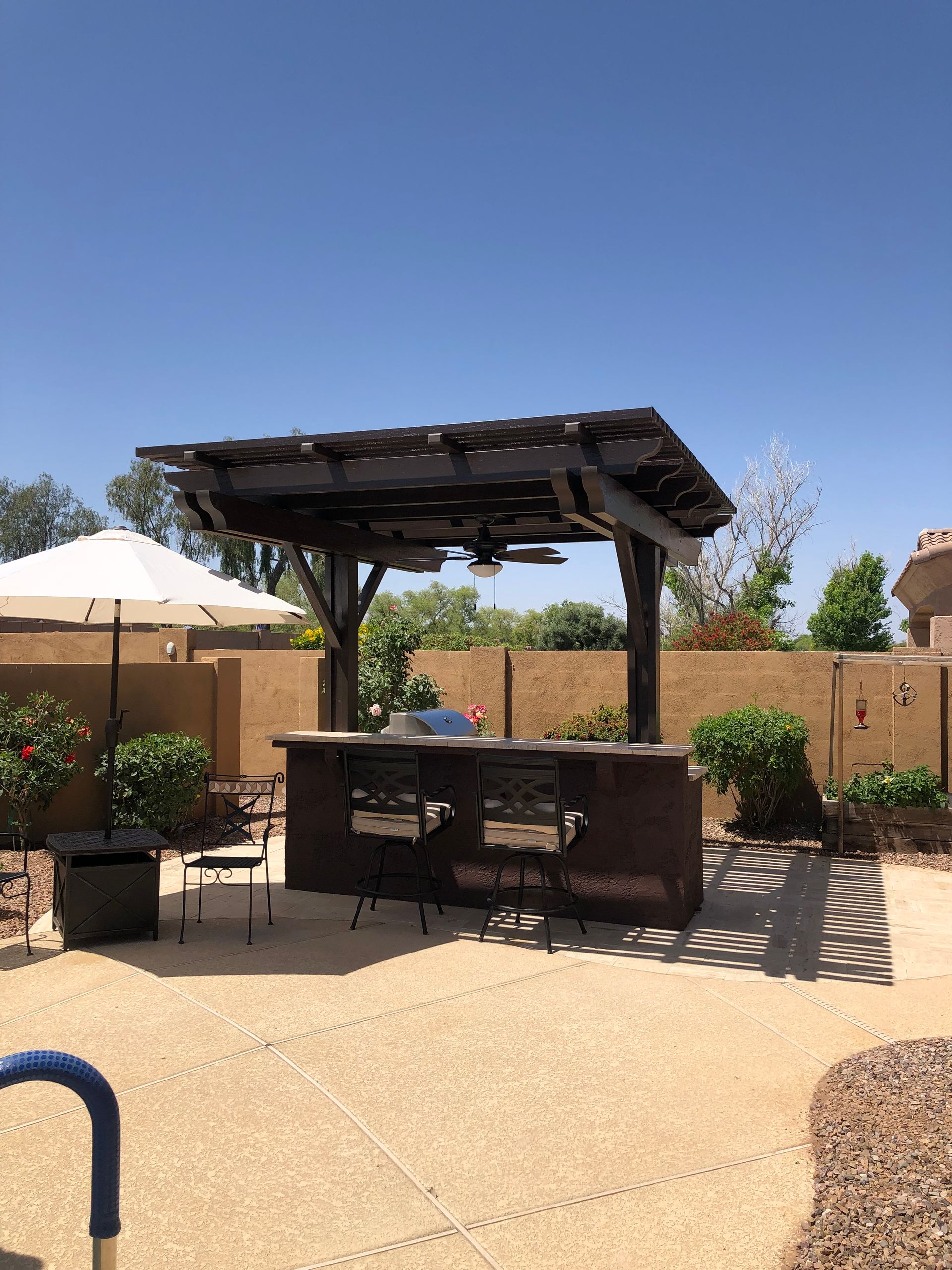 Outdoor kitchen with a pergola, bar seating, and grill by a pool.