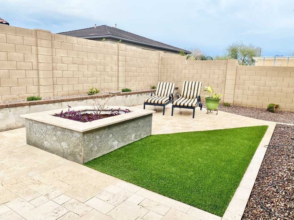 Patio with fire pit, two chairs, and artificial grass against a block wall.
