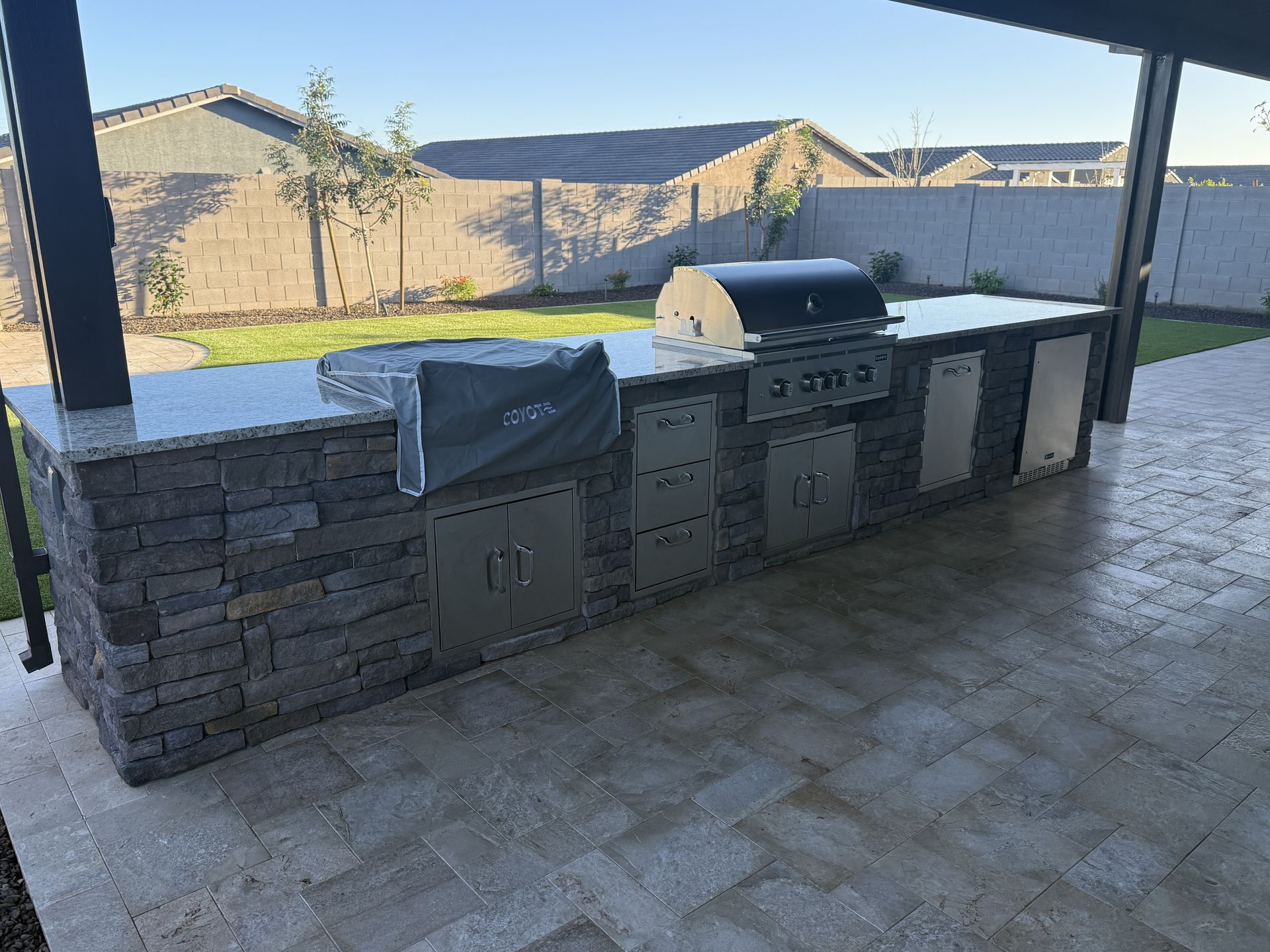 Outdoor kitchen with a stone facade, granite countertop, grill, and storage cabinets.