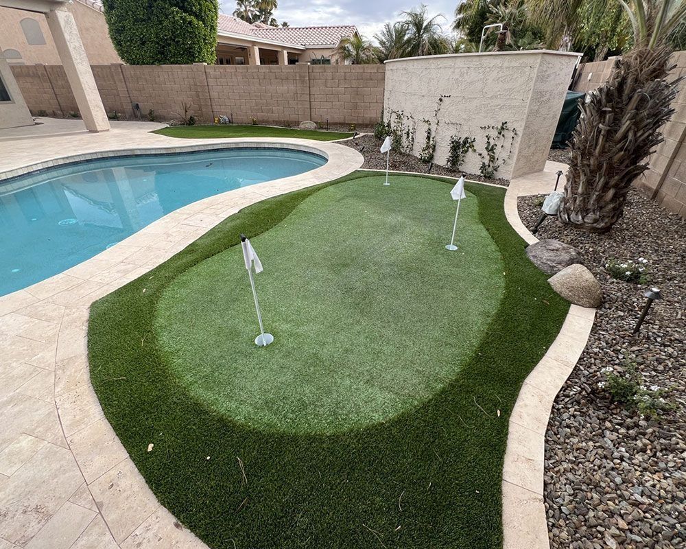 Backyard putting green next to a pool. Artificial turf, three holes with flags.