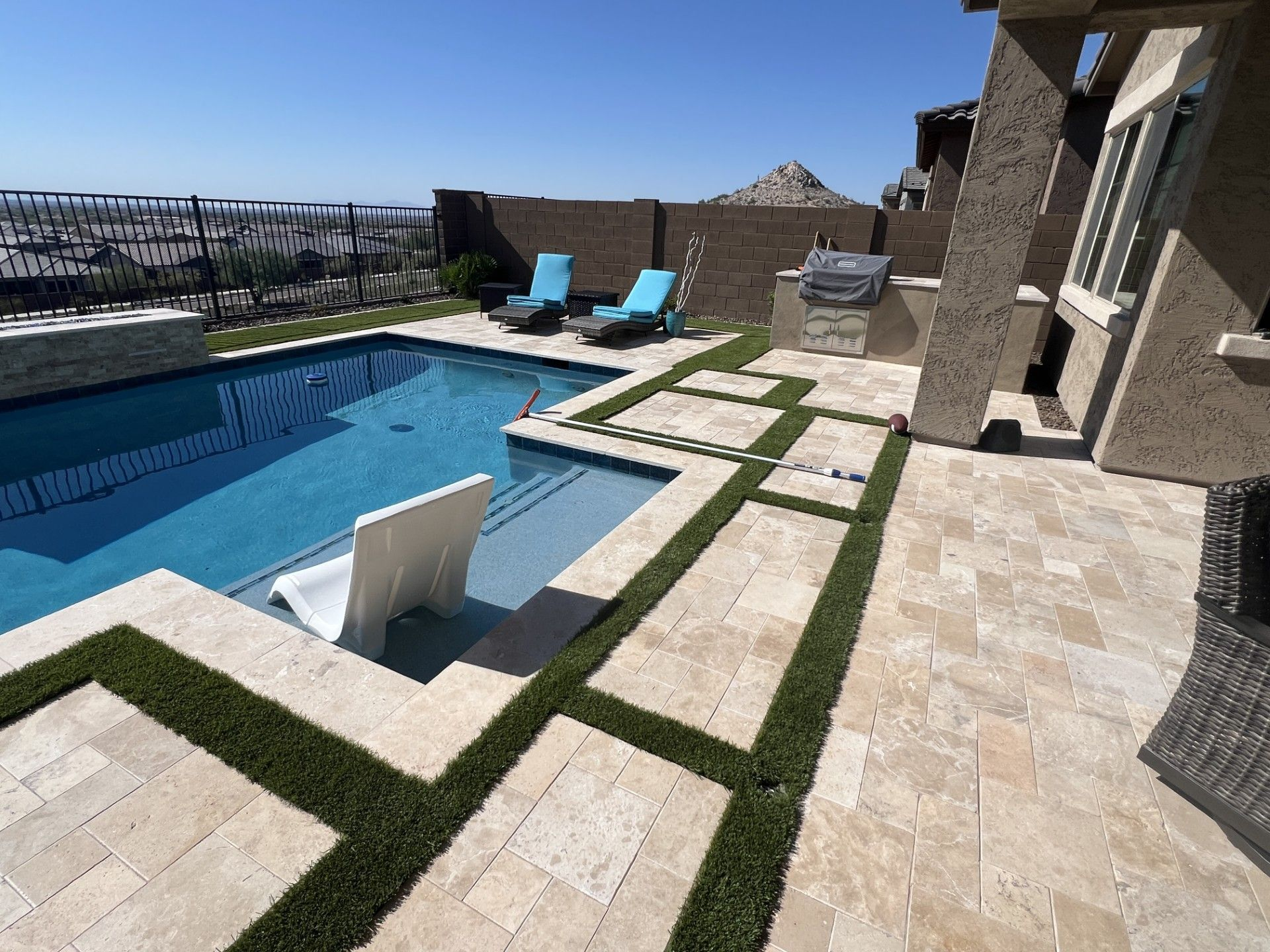 Poolside patio with pool, lounge chairs, built-in grill, and grass accents.
