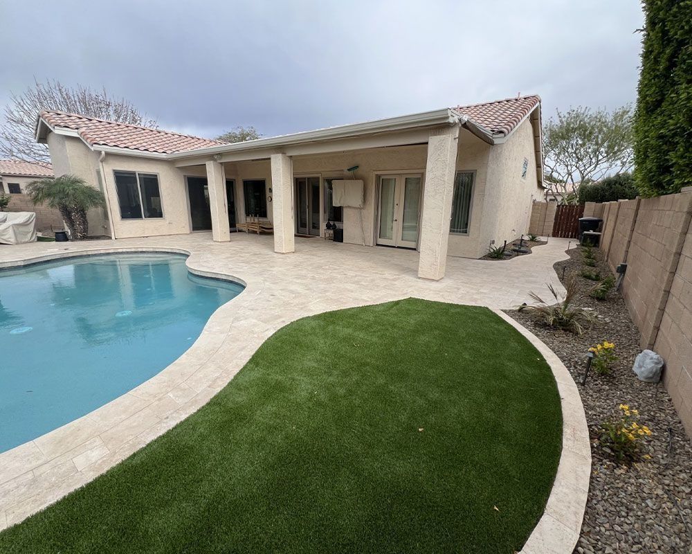 Backyard with pool, patio, and green lawn. Tan stucco house and fence with plants. Blue pool water.