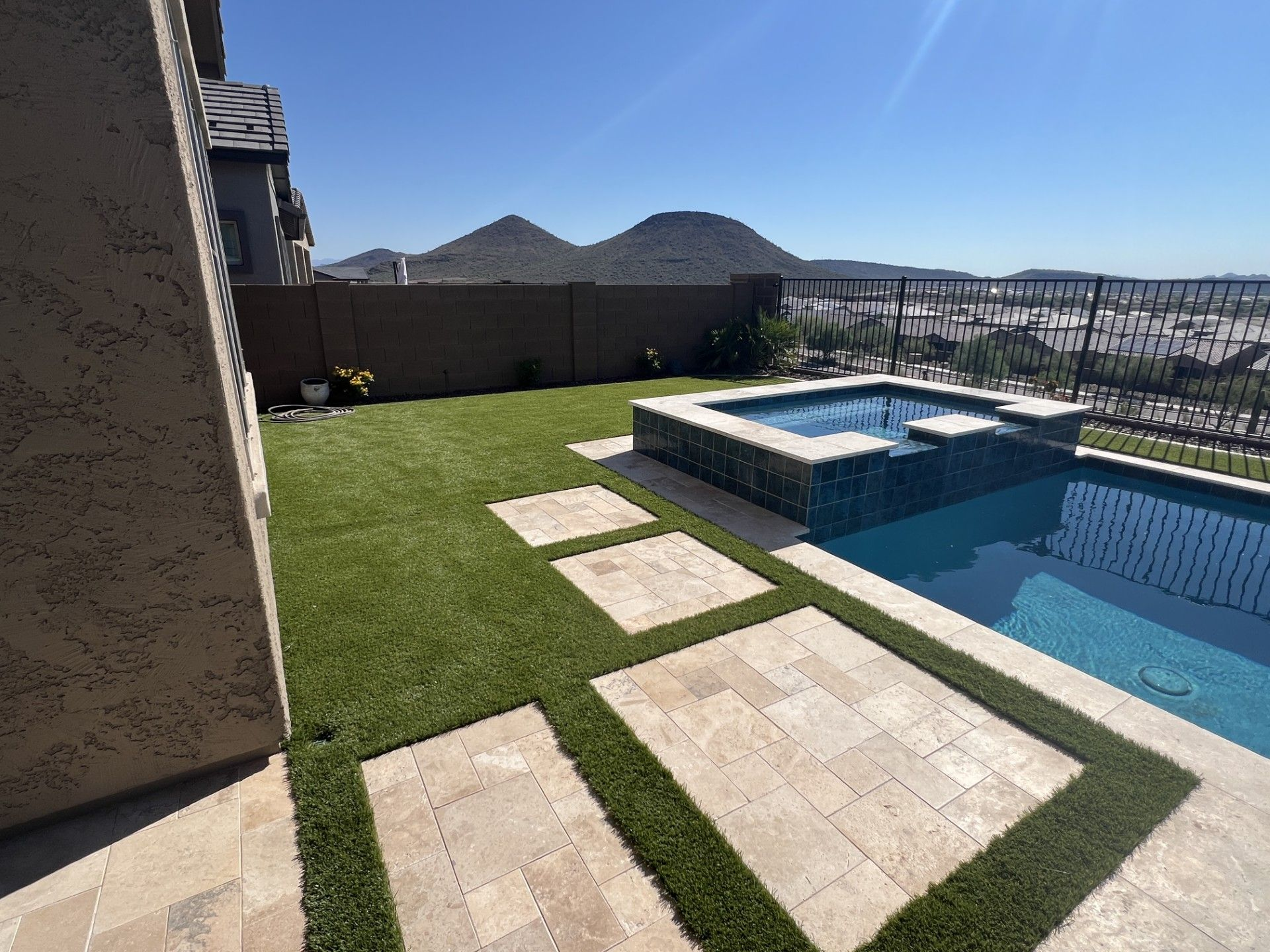 Backyard with pool, hot tub, and artificial grass with stepping stones; a desert mountain backdrop.
