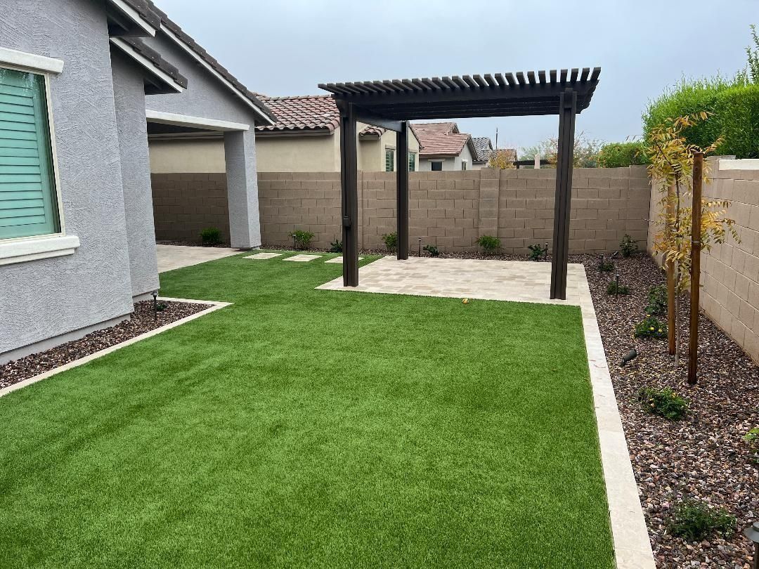 Backyard with artificial grass, a pergola, and a concrete patio on a cloudy day.