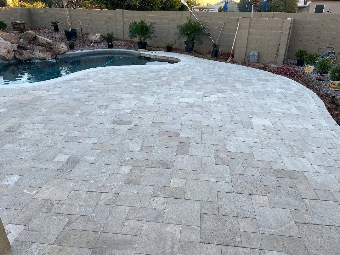 Patio paved with light stone surrounding a blue pool, and landscaping.