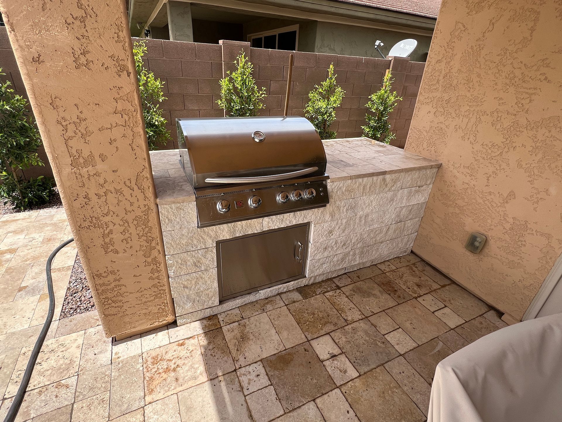 Outdoor kitchen with a stainless steel grill and a beige stone countertop.