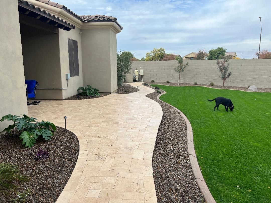 Beige stone path curves through yard with green grass and black dog sniffing.