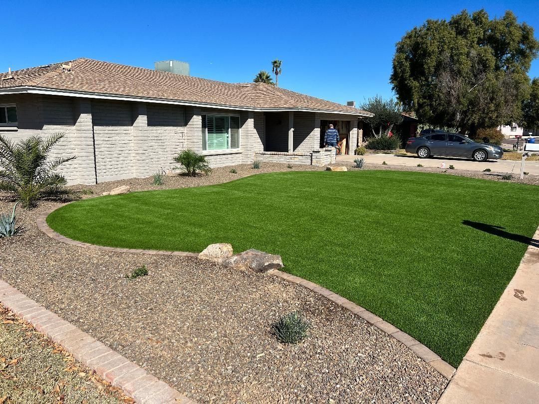 House with green lawn and brown brick border.  Low-lying plants and blue sky.
