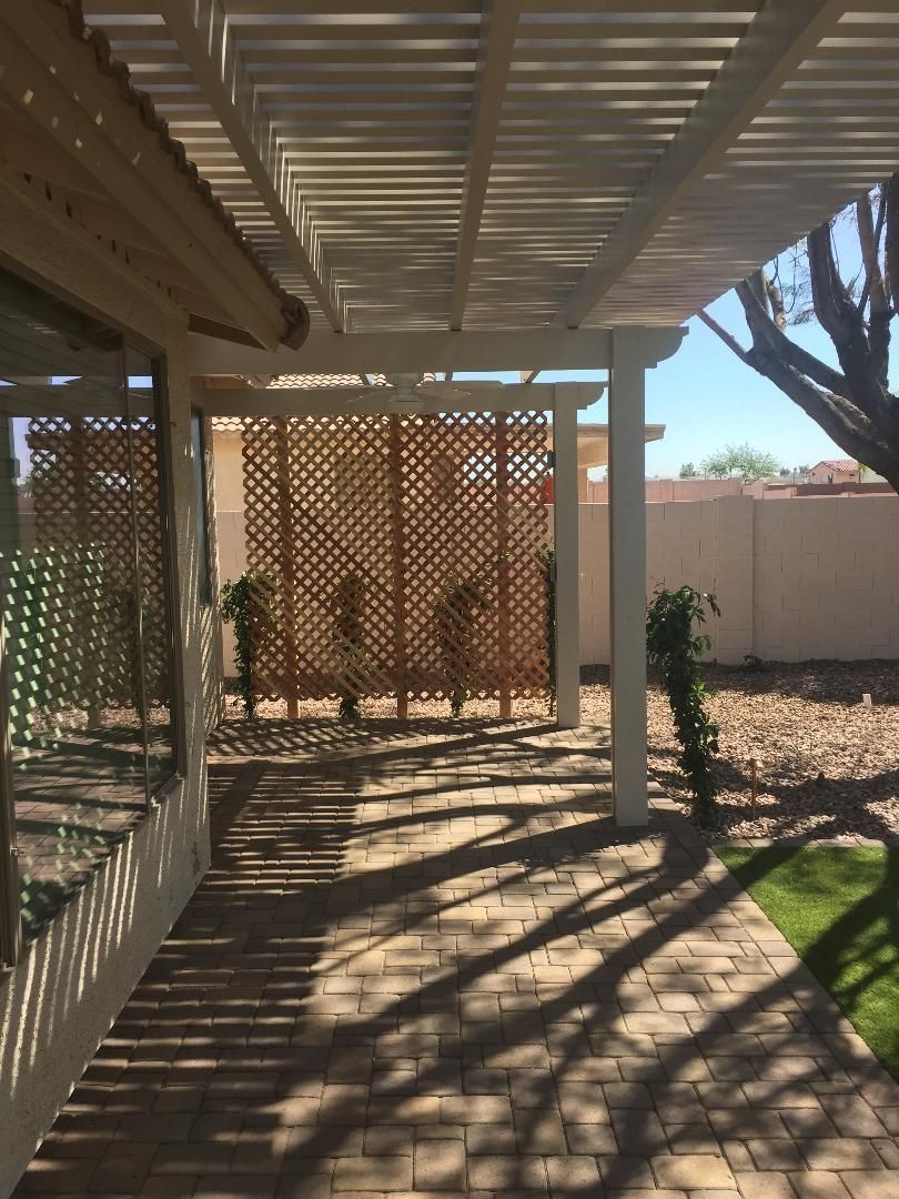 Patio with a pergola, brick pavers, and a wooden screen, casting shadows on a sunny day.