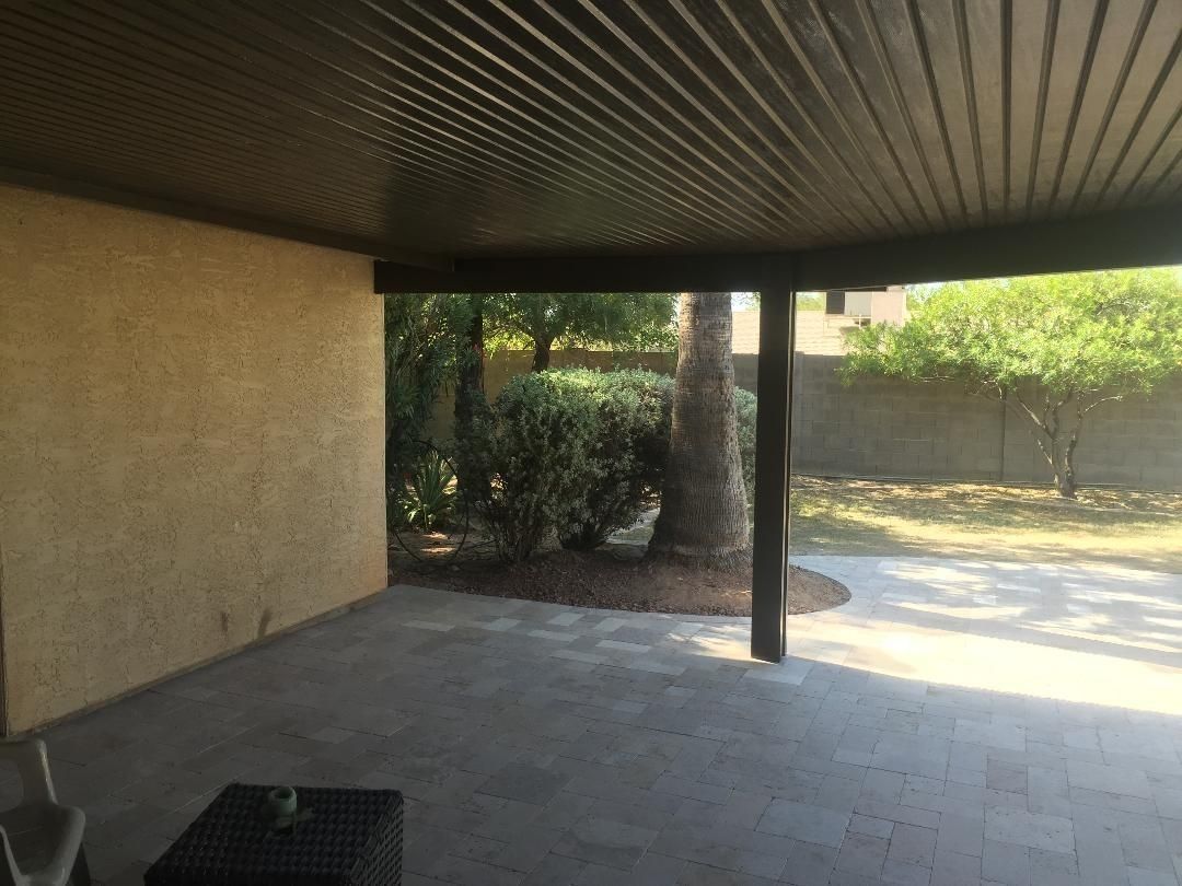Covered patio with a stone floor and a view of a backyard with trees and a fence.