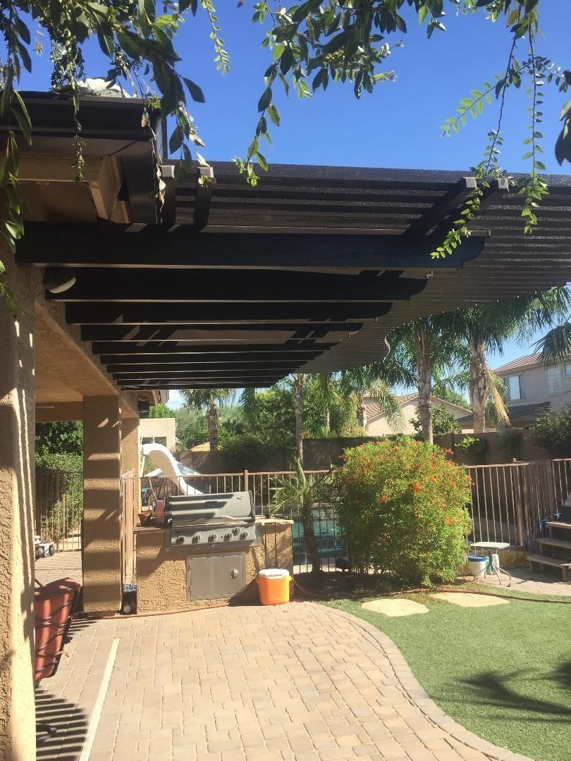Outdoor patio with a grill under a dark wooden pergola, sunny day.