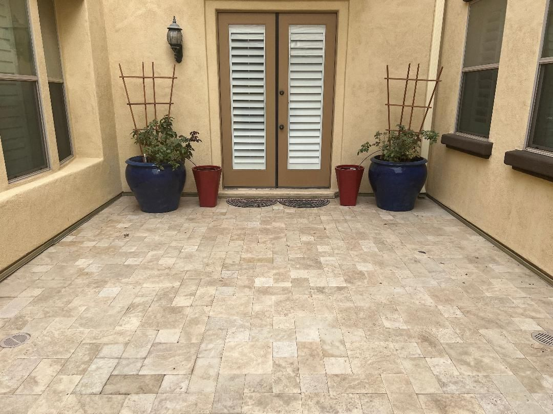 Stone patio with potted plants, double doors with shutters, and a cream-colored building exterior.