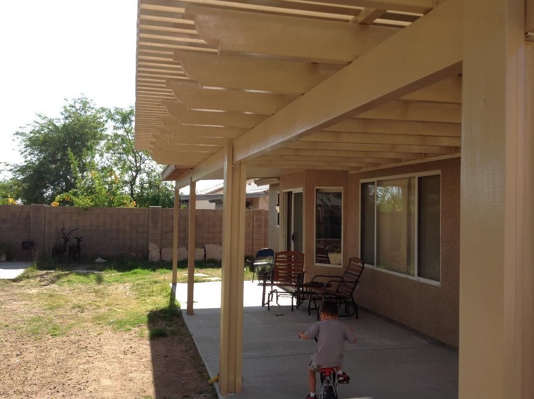 Covered patio with a child riding a bike, adjacent to a house and backyard.