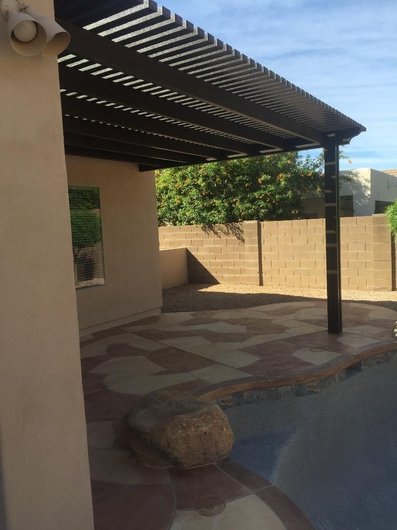 Patio with stone pavers, pergola, and wall next to a pool.
