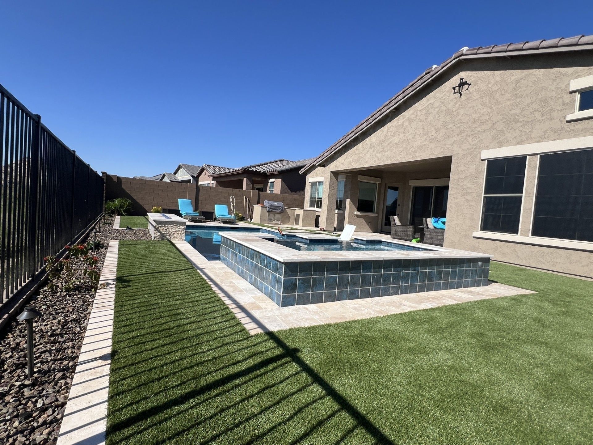 Backyard with pool and spa, surrounded by grass and a fence, sunny day.