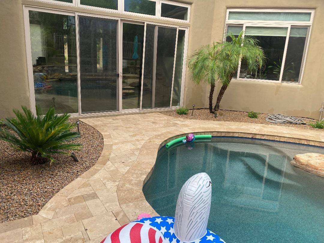 Backyard with pool, stone path, glass doors, small trees, and inflatable pool toy.