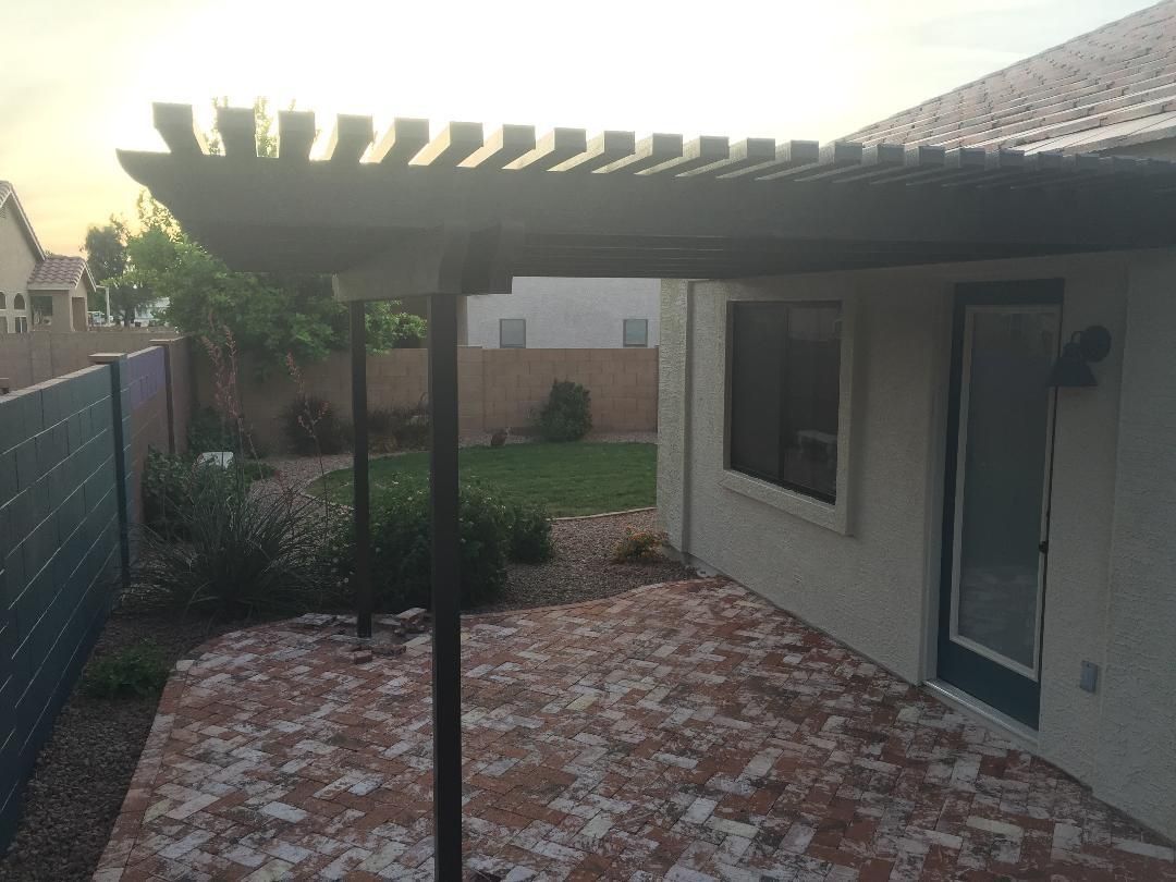 Patio with a pergola, brick pavers, and a door, in a backyard setting.