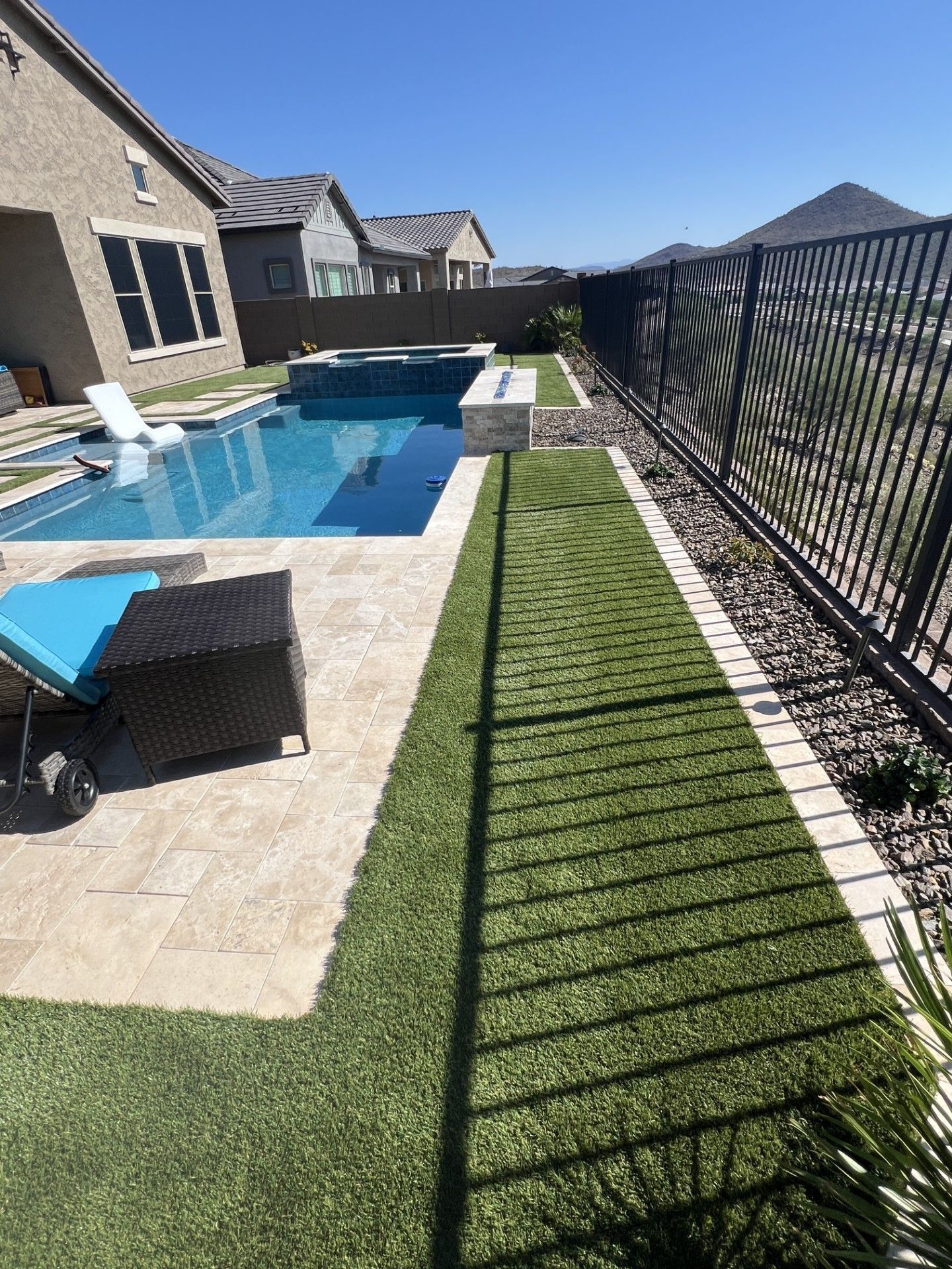 Backyard with a swimming pool, artificial grass, black fence, and lounge chair. Sunny day.