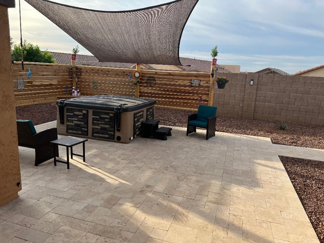 Hot tub on a stone patio with shade sail, privacy fence, and seating.