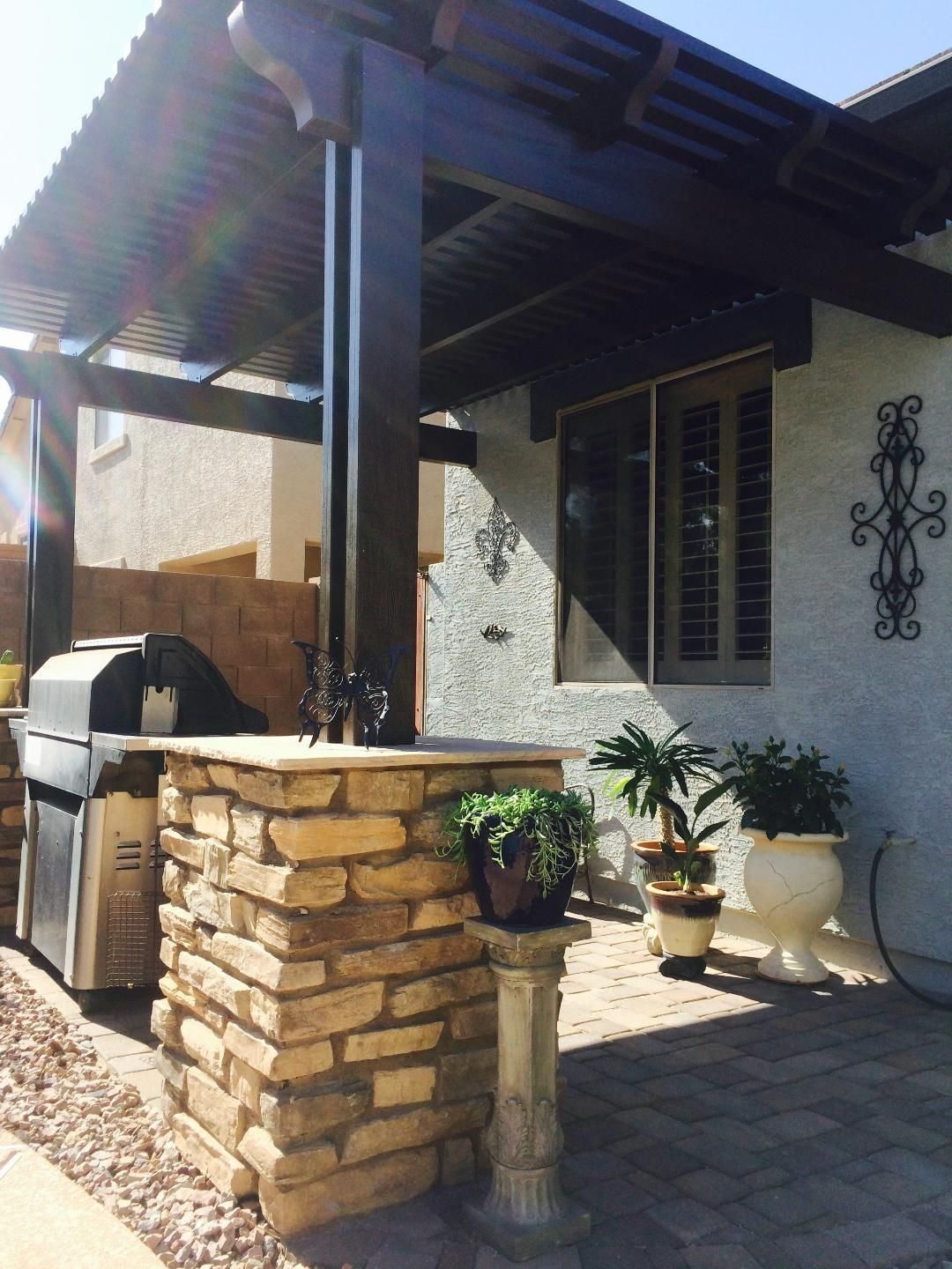 Outdoor patio with stone grill island, wooden pergola, and potted plants.