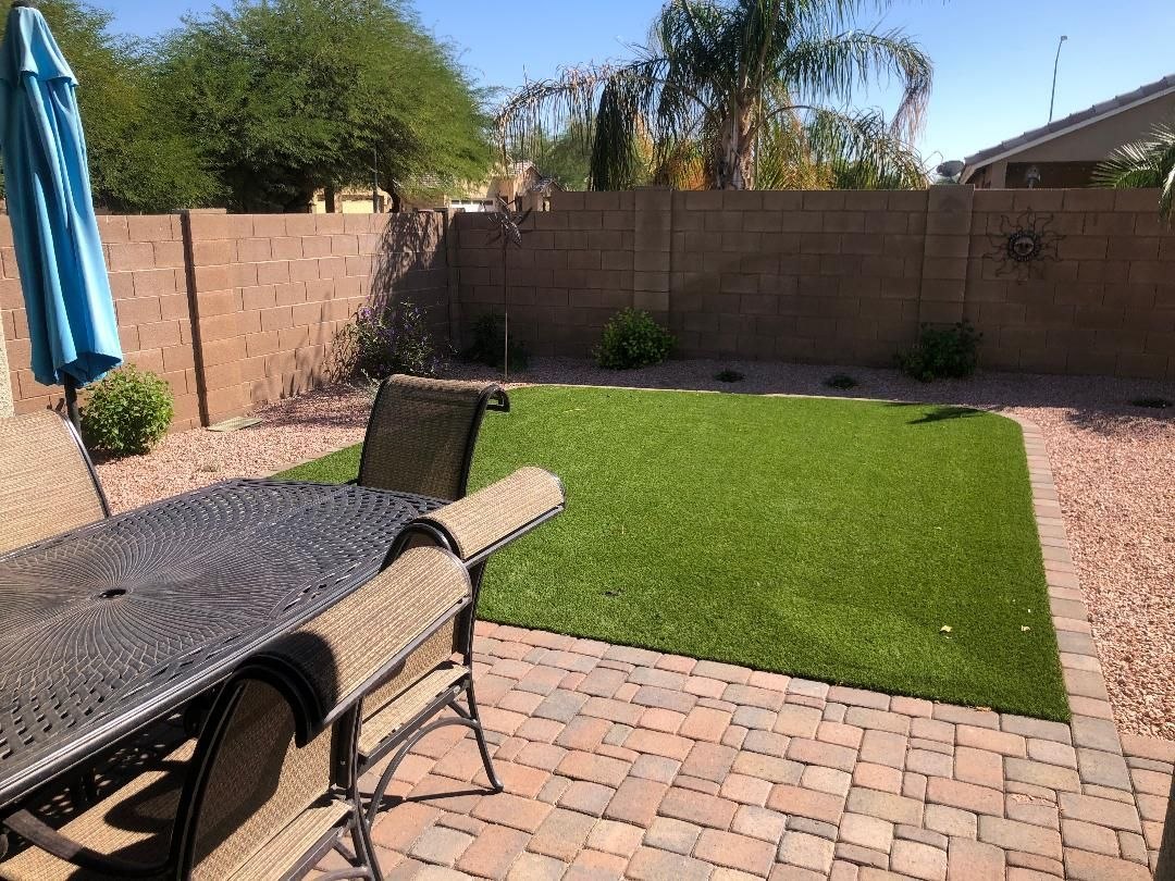 Patio with brick pavers, artificial grass, and a dining table with chairs next to a block wall.