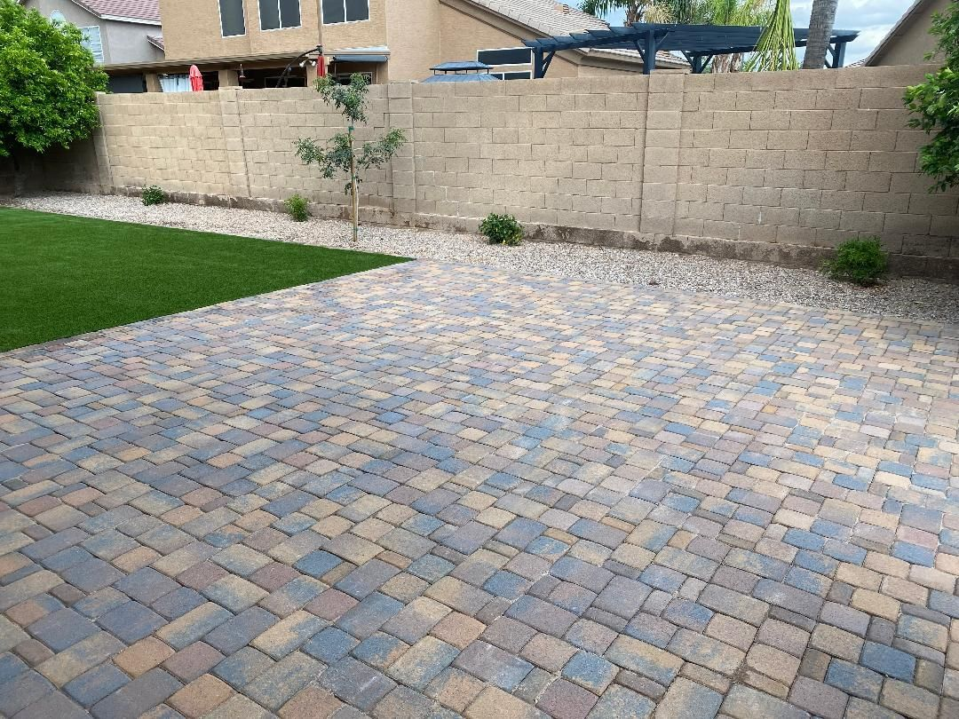 Patio paved with multi-colored bricks adjacent to a patch of green grass; a wall in the background.