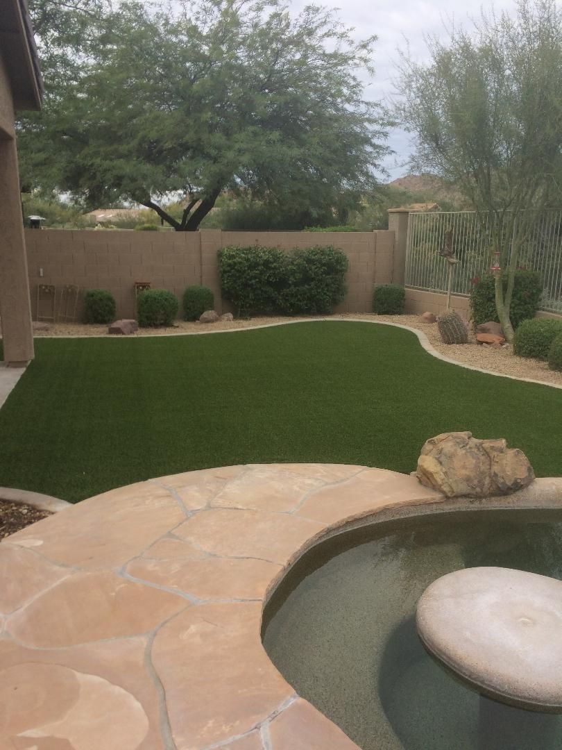 Patio with stone pavers, pool, and green lawn surrounded by landscaping.