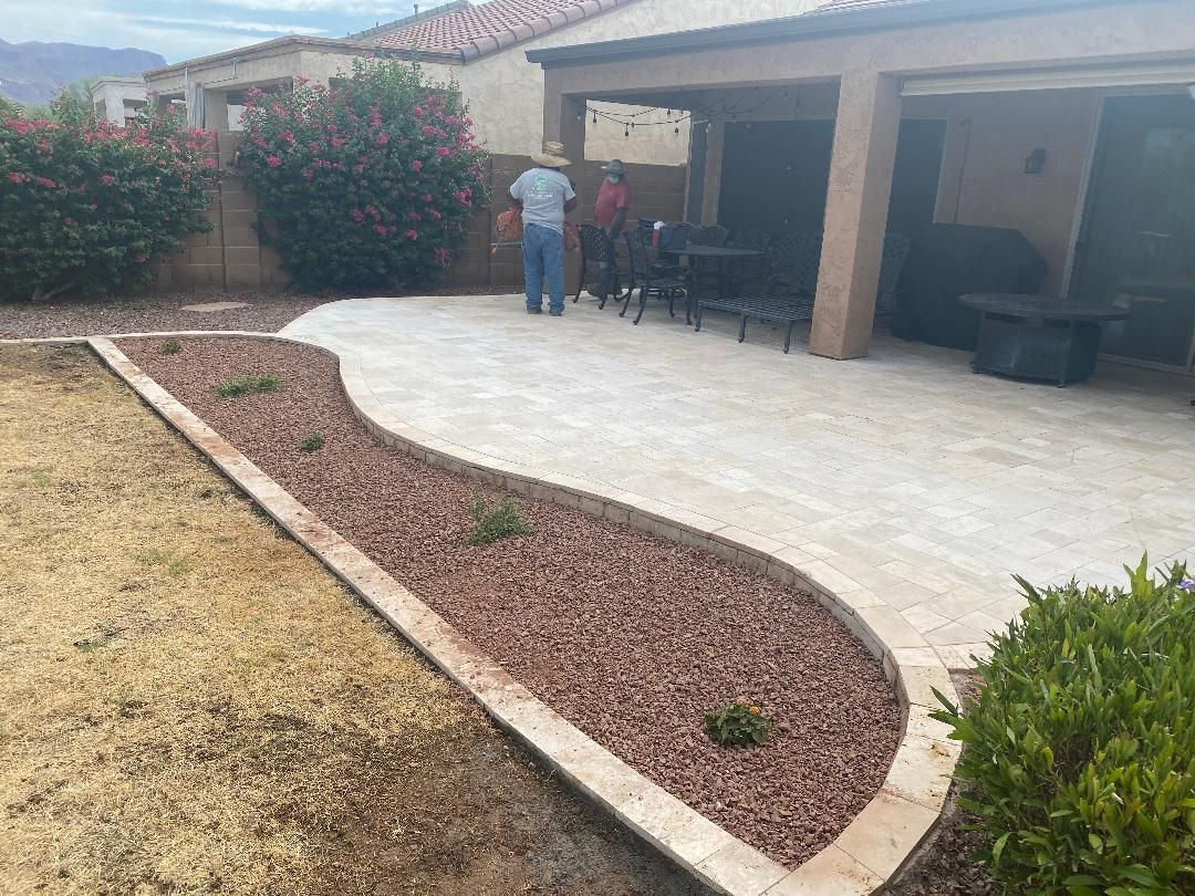 Backyard with a gravel patio, rock bed, and person standing under an awning.