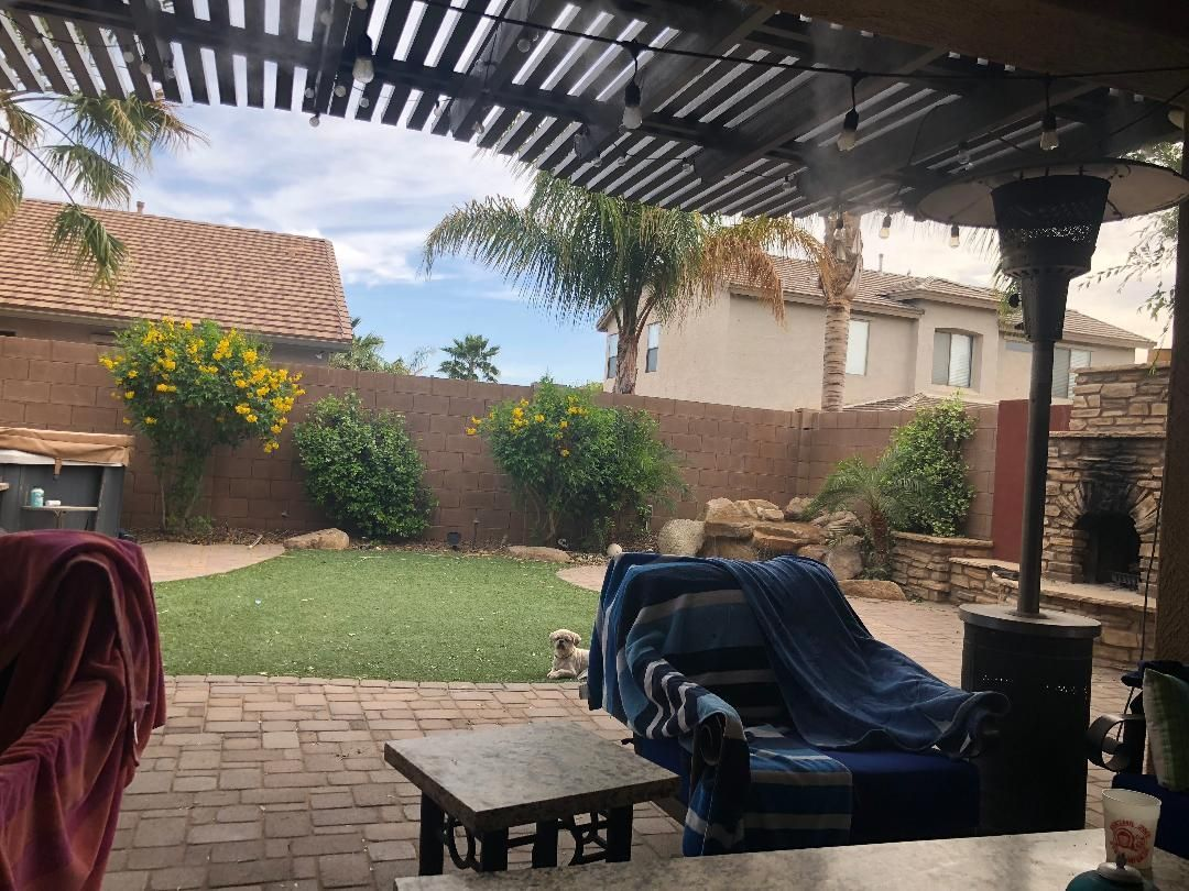 Backyard patio with lawn, seating, and heating lamp under a pergola.