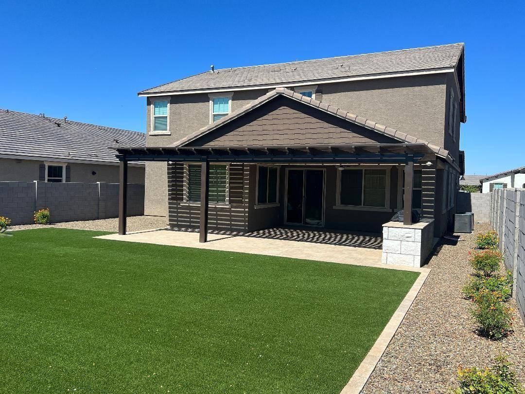 Backyard with pergola, house, green lawn, and blue sky.