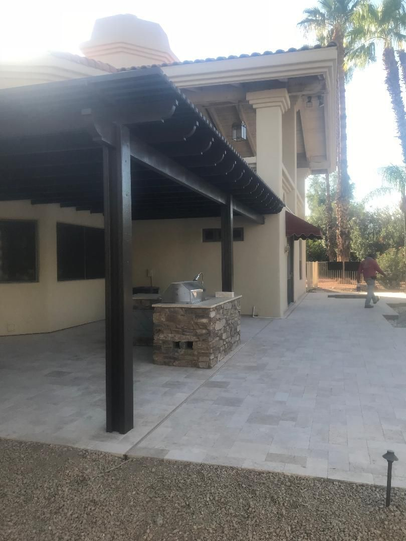 Patio with pergola, outdoor kitchen, and stone facade, next to a beige building.